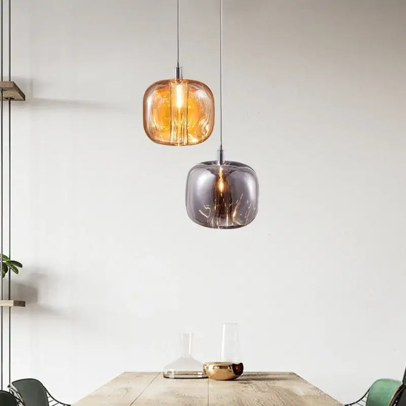 Two modern pendant lights with amber and smoky gray glass shades hang above a wooden table decorbites light luxury crystal