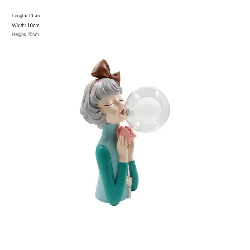 A modern gray and gold decorbites bubble girl statue featuring a resin girl ornament with silver hair and teal dress blowing a bubble