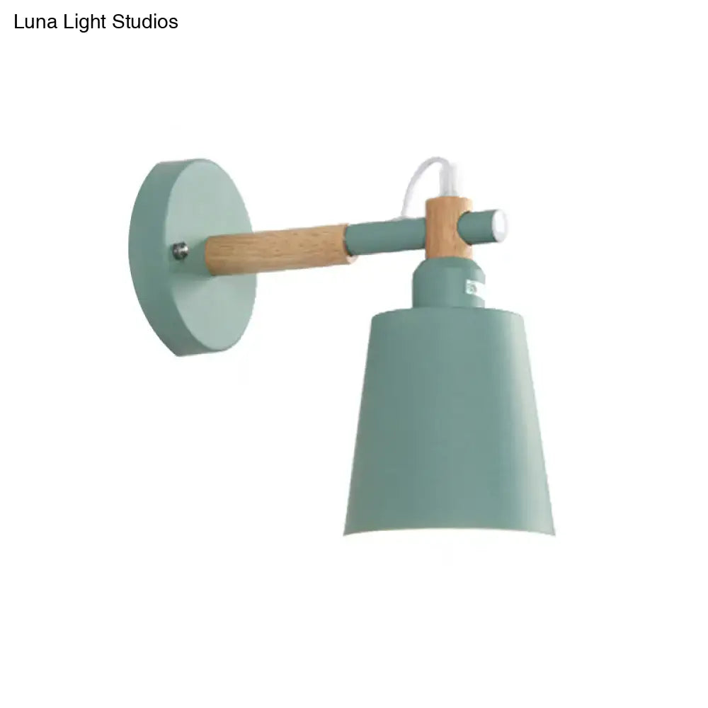 A modern wall sconce light with a matte sage green metal shade and wooden arm for bedroom lighting