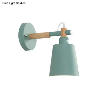A modern wall sconce light with a matte sage green metal shade and wooden arm for bedroom lighting