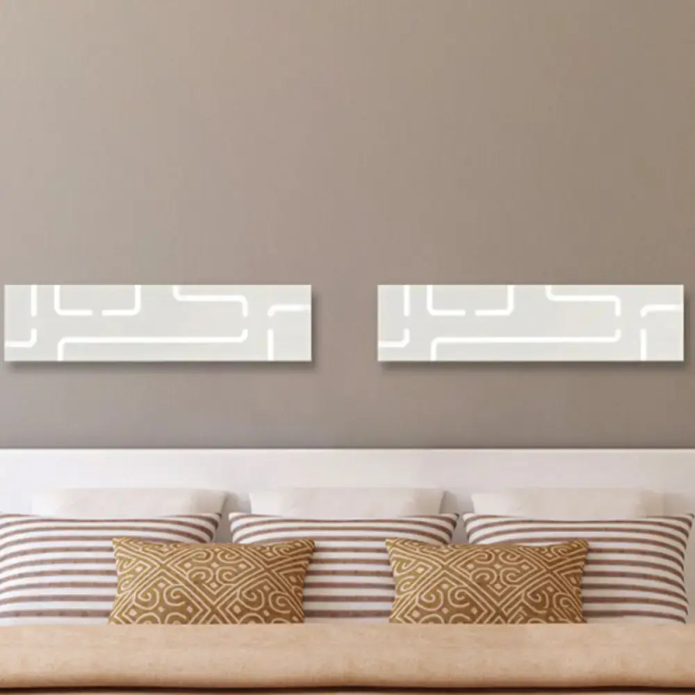 Two rectangular white wall art pieces with minimalist geometric patterns above a bed in warm white light