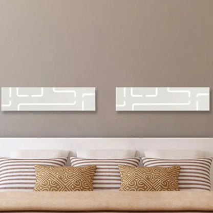 Two rectangular white wall art pieces with minimalist geometric patterns above a bed in warm white light