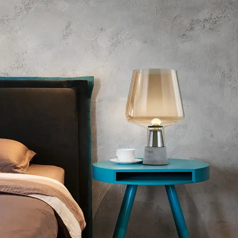 A modern table lamp with leimu amber glass shade and sleek metallic base on a vibrant blue side table for bedroom decorbites leimu amber
