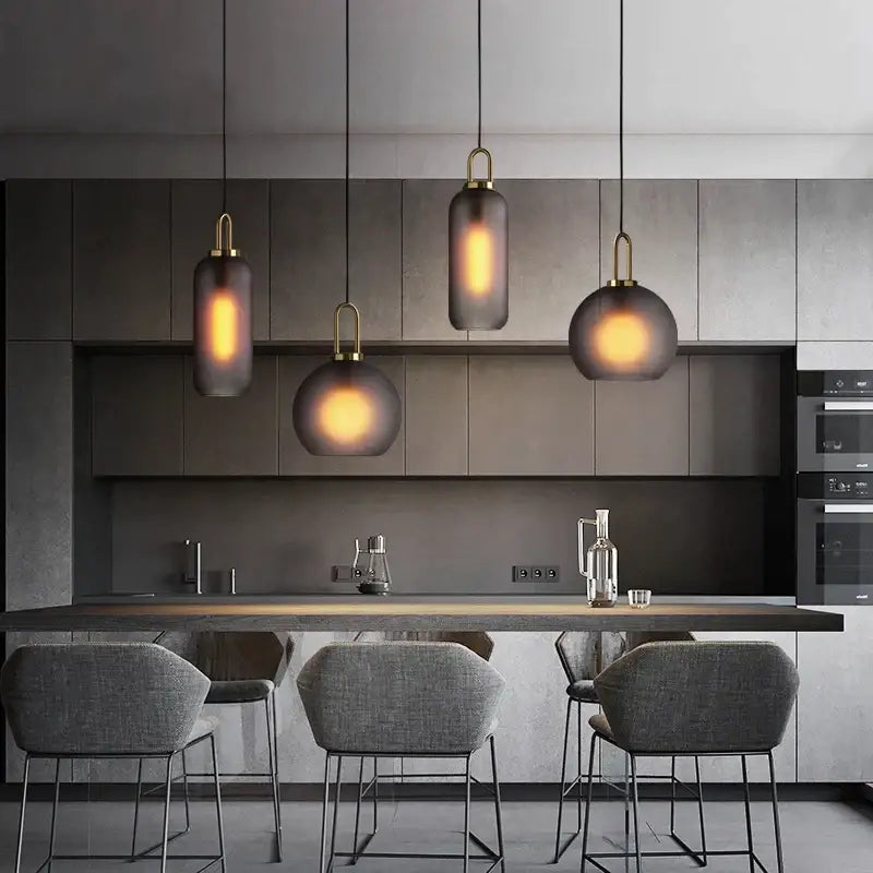 Four modern gray decorbites glass ball pendant lights with smoked glass and brass accents hang above kitchen island