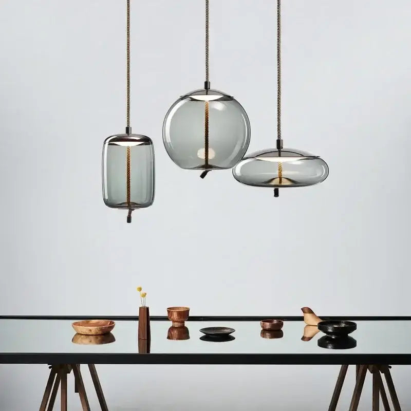Three modern gray glass chandelier knot pendant lights with translucent shades and brass cords over a dining table