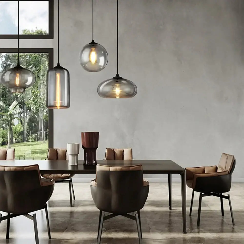 Three modern gray glass pendant lights with frosted and clear finishes hang above a dining table