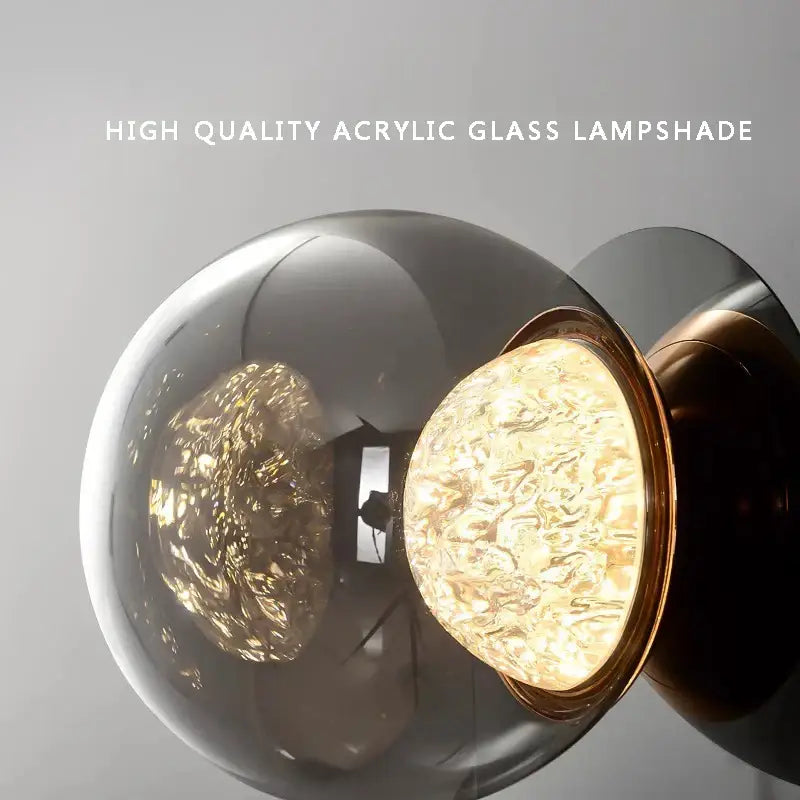 A sleek modern gray glass wall light with a translucent smoke-gray acrylic lampshade and polished brass rim