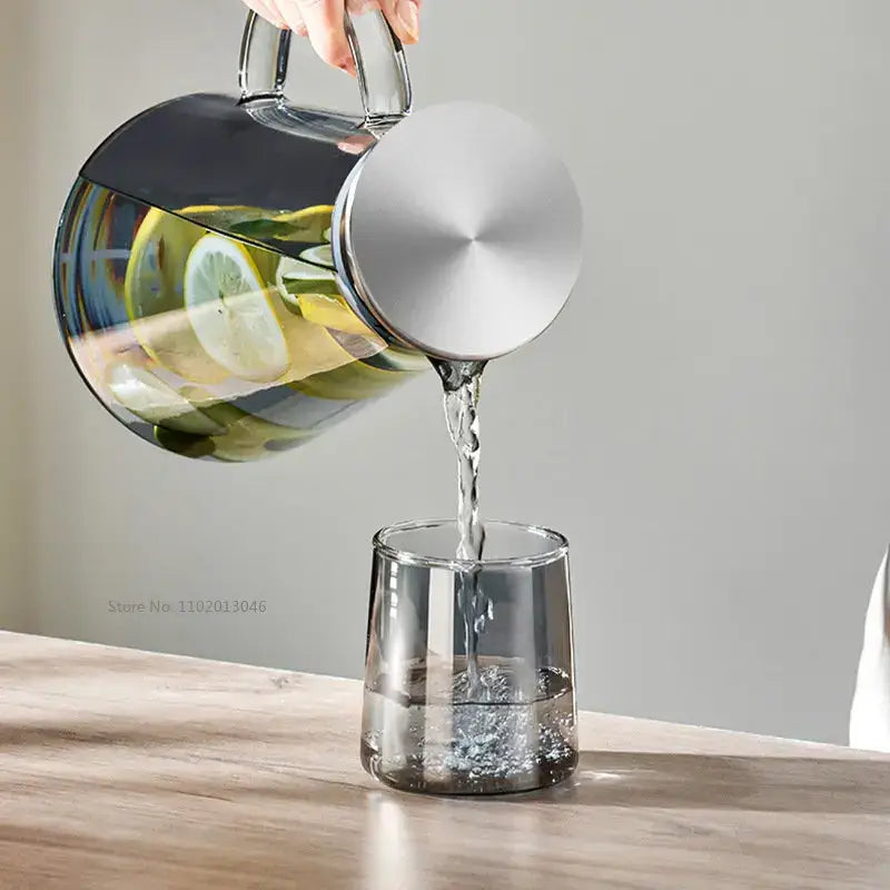 A sleek modern gray glass water pitcher with brushed stainless steel lid and handle pouring into a matching glass