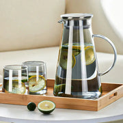 Modern gray glass water pitcher with stainless steel lid and handle filled with water and sliced lemons