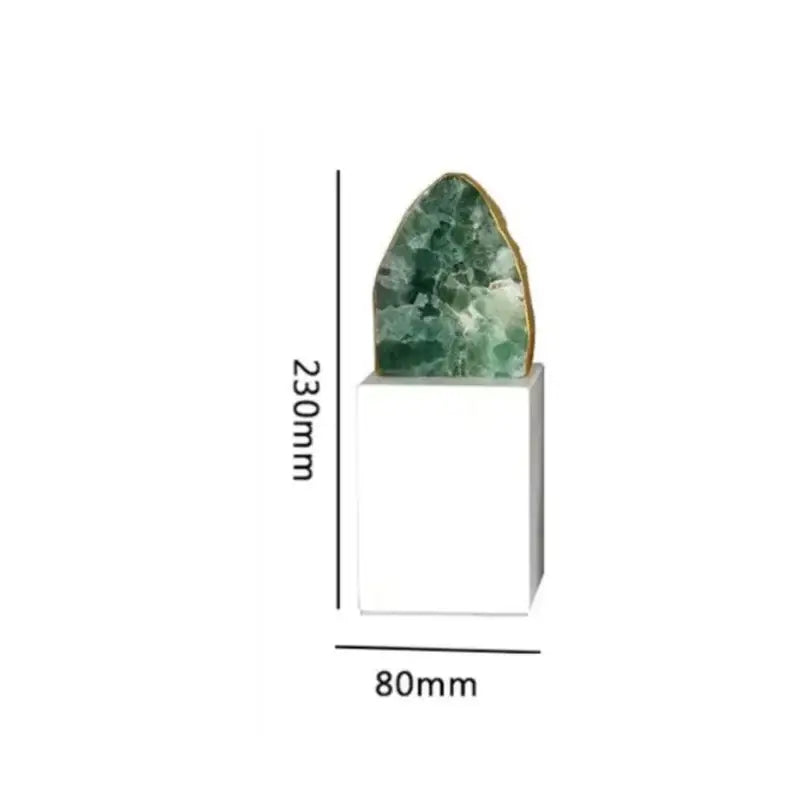 A polished green agate crystal stone slice with a golden rim on a white ceramic pedestal for living room decor
