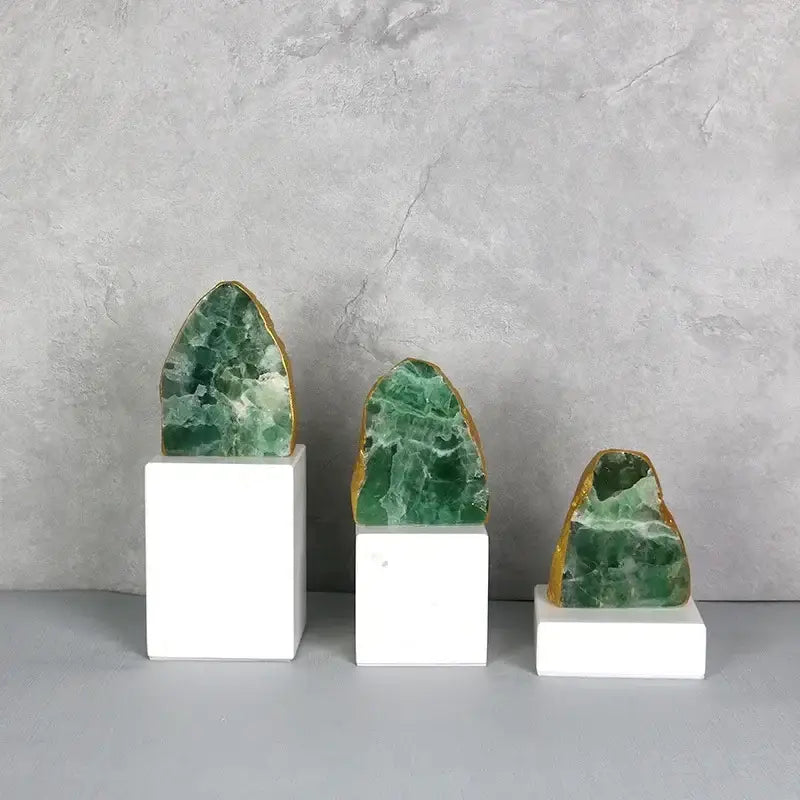 Set of three green agate crystal geode slices with gold-edged rims on white pedestals for modern decor