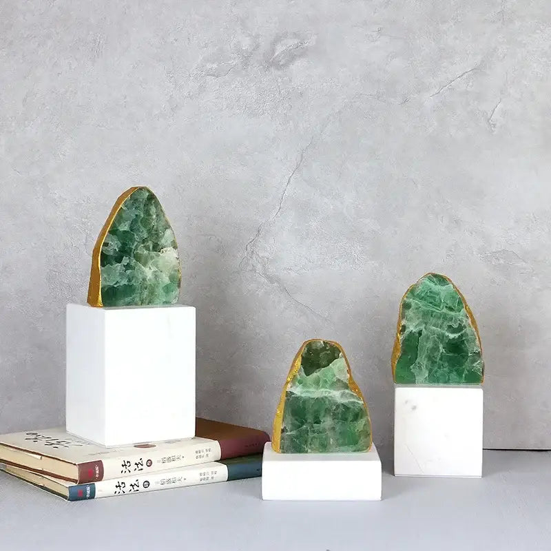 Three green agate crystal stone bookends with gold-edged surfaces on white marble bases for living room decor