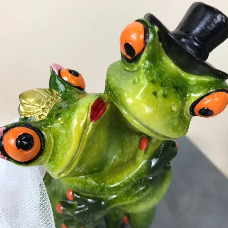 Modern green and orange leggy frog couple figurine decorbites with a green ceramic frog wearing a black top hat holding a gold crown
