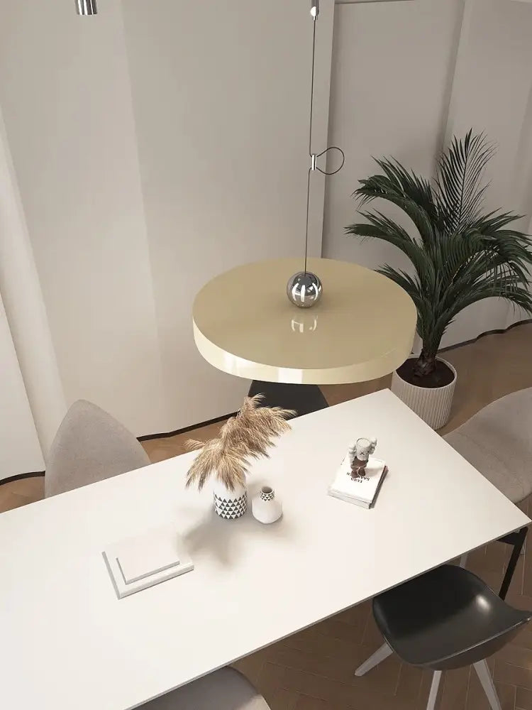 Modern green curved pendant light chandelier above a sleek beige round table with minimalist black legs in dining room