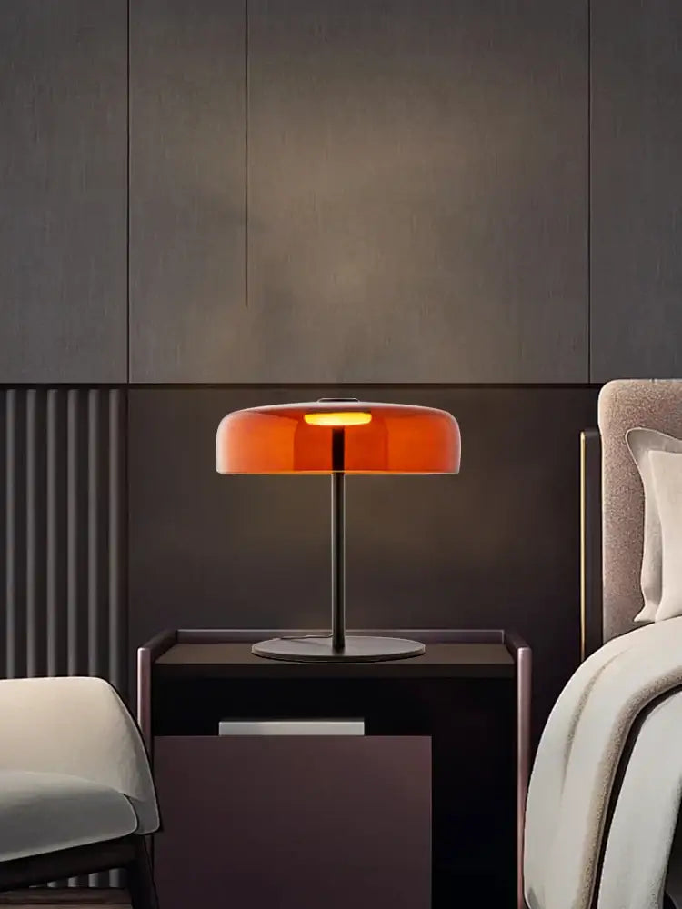 A modern table lamp with a translucent orange glass shade and slender black metal base for bedroom use