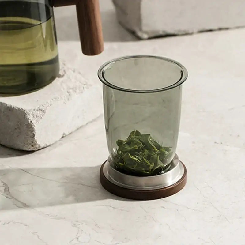Modern green and gray decorbites glass tea cup with wood handle and translucent infuser holding loose green tea leaves