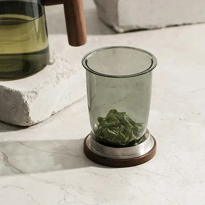 Modern green and gray decorbites glass tea cup with wood handle and translucent infuser holding loose green tea leaves