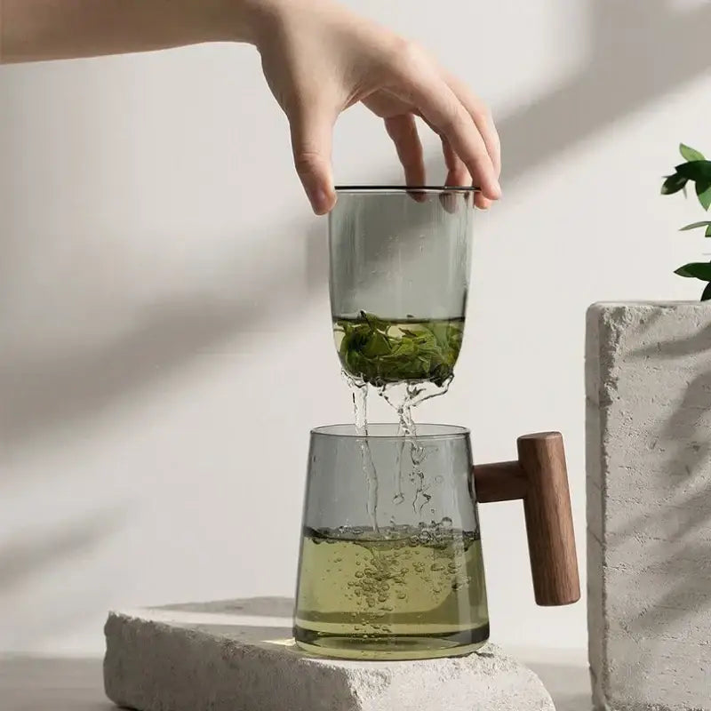 A modern green and gray glass tea cup with wood handle filled with green tea leaves from decorbites glass tea set