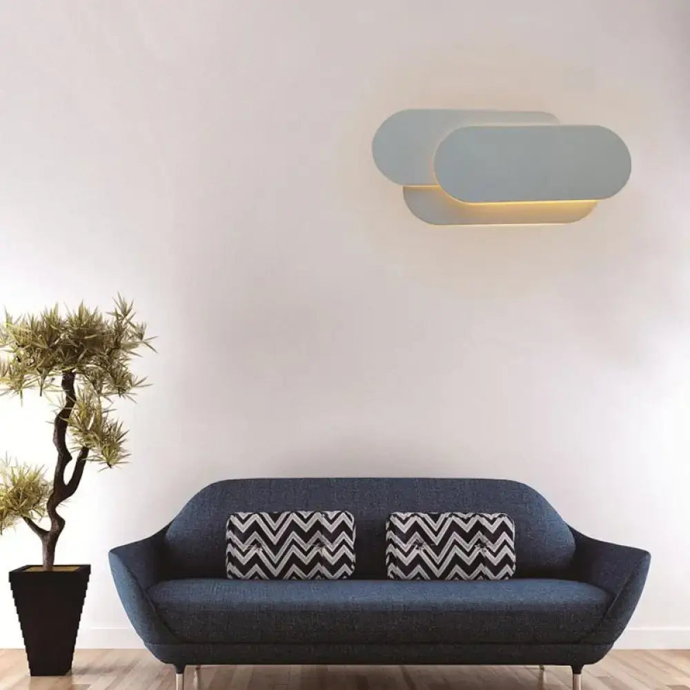 Modern grey oval metal sconce with two overlapping matte light gray shades emitting warm bedroom LED light