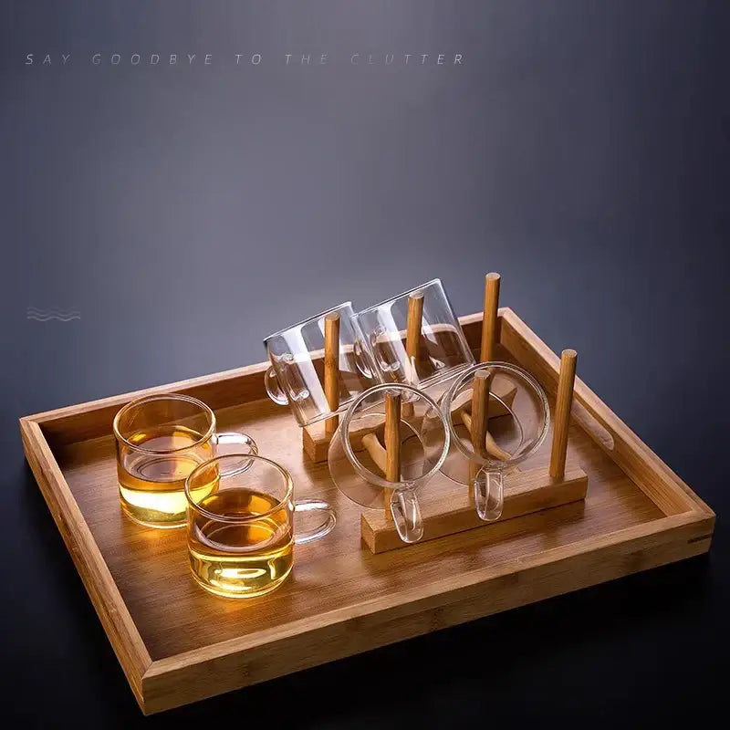 Modern heat resistant clear glass tea cup set with handles filled with golden tea on wooden tray with bamboo holders