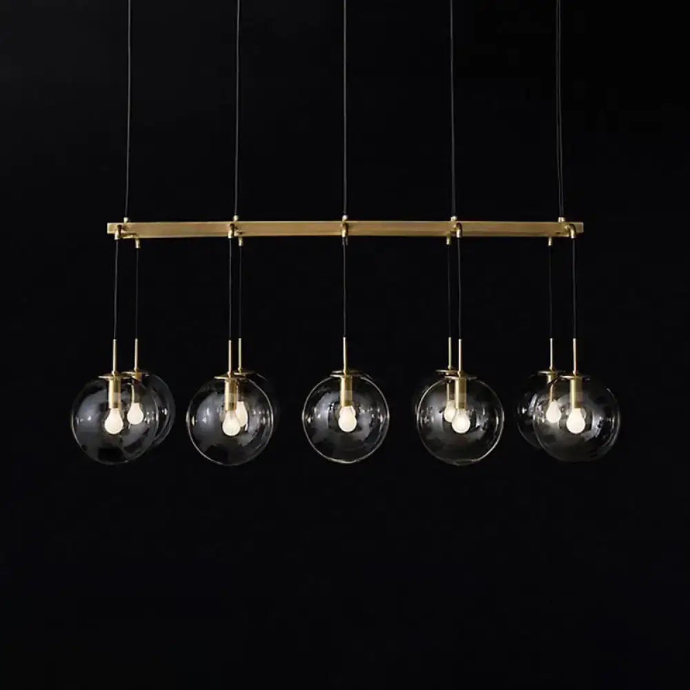Modern brass bar pendant light with five clear glass globe shades for industrial smoke glass island lighting use