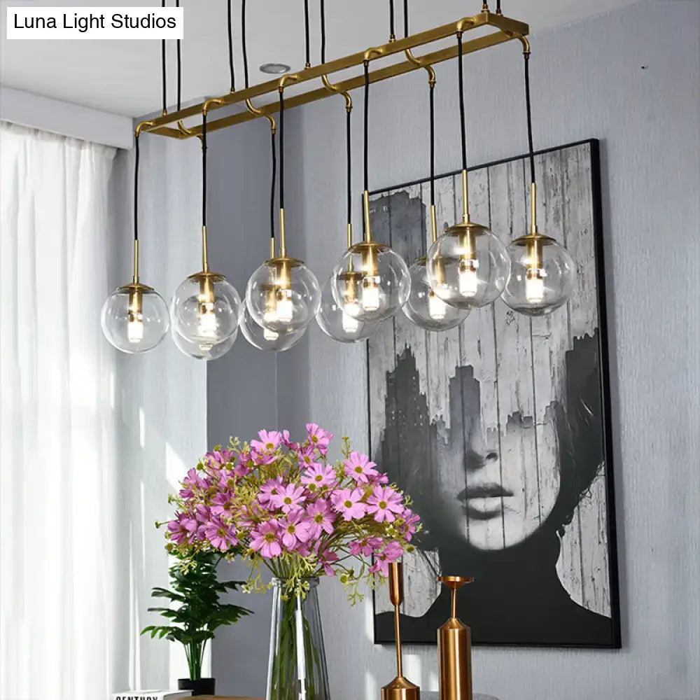 Gold-toned industrial smoke glass island lighting pendant fixture with clear glass globe shades and black cords by DecorBites