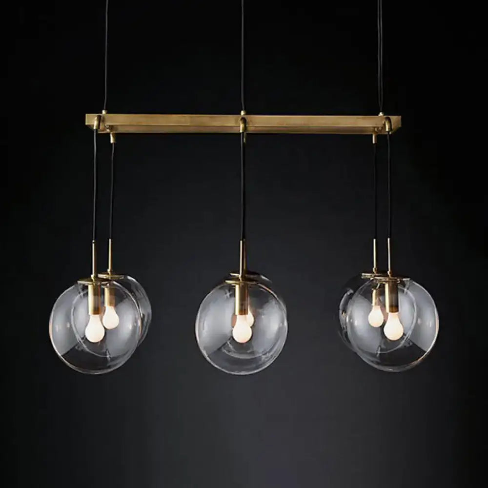 Brass bar pendant light with three clear smoke glass globe shades and exposed bulbs for industrial island lighting