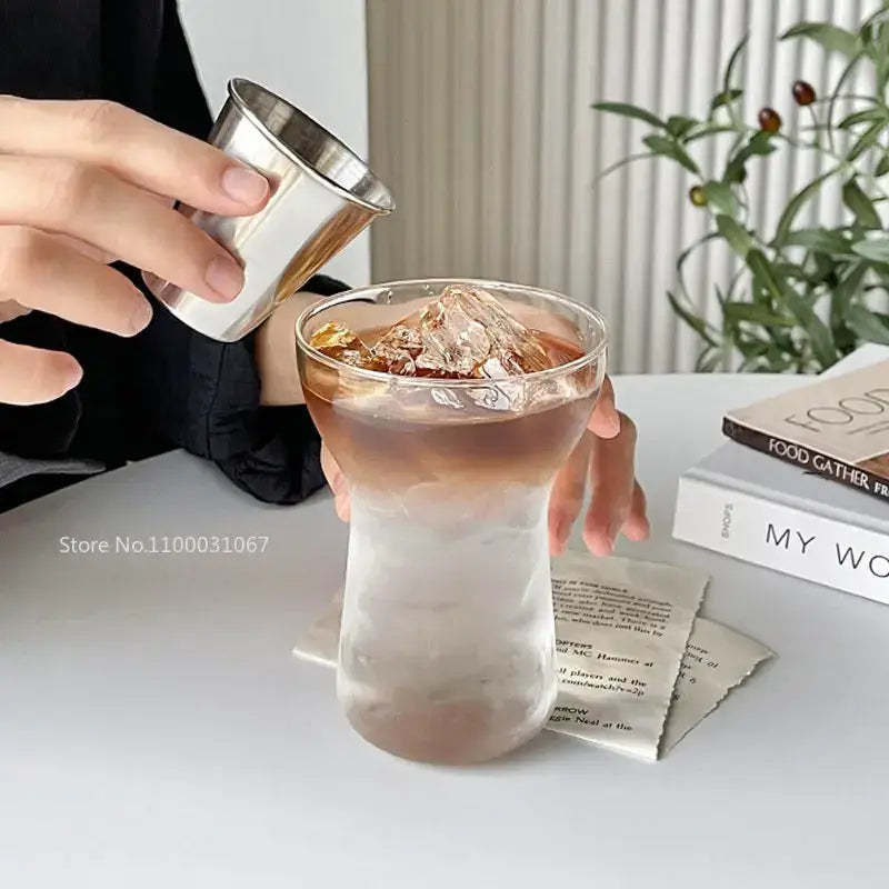 A sleek stainless steel jigger pouring dark liquid into a modern insulated decorbites glass drink cup set