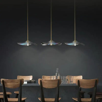 Three elegant translucent blue glass plated pendant lamps with gold fixtures hanging above a dining table