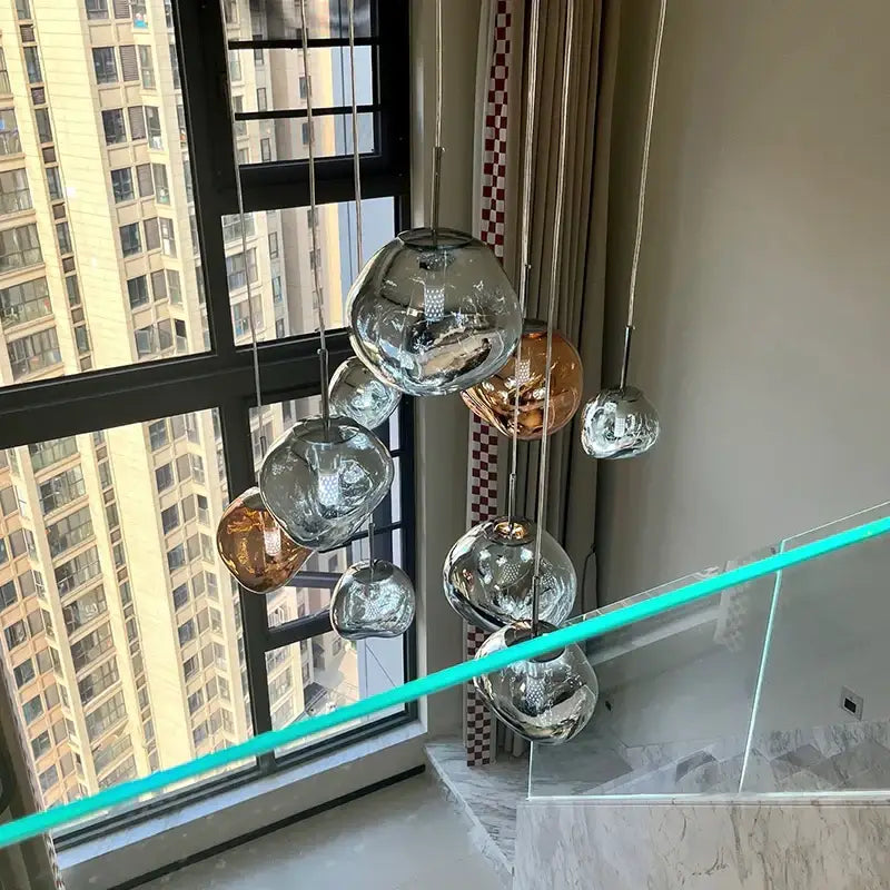 A modern lava glass pendant light set with spherical orbs in amber and silver suspended on polished chrome rods