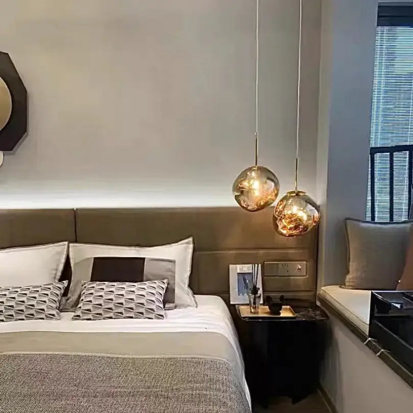 Two spherical gold finished pendant lights with polished chrome finish hang above a bed in a modern dining room