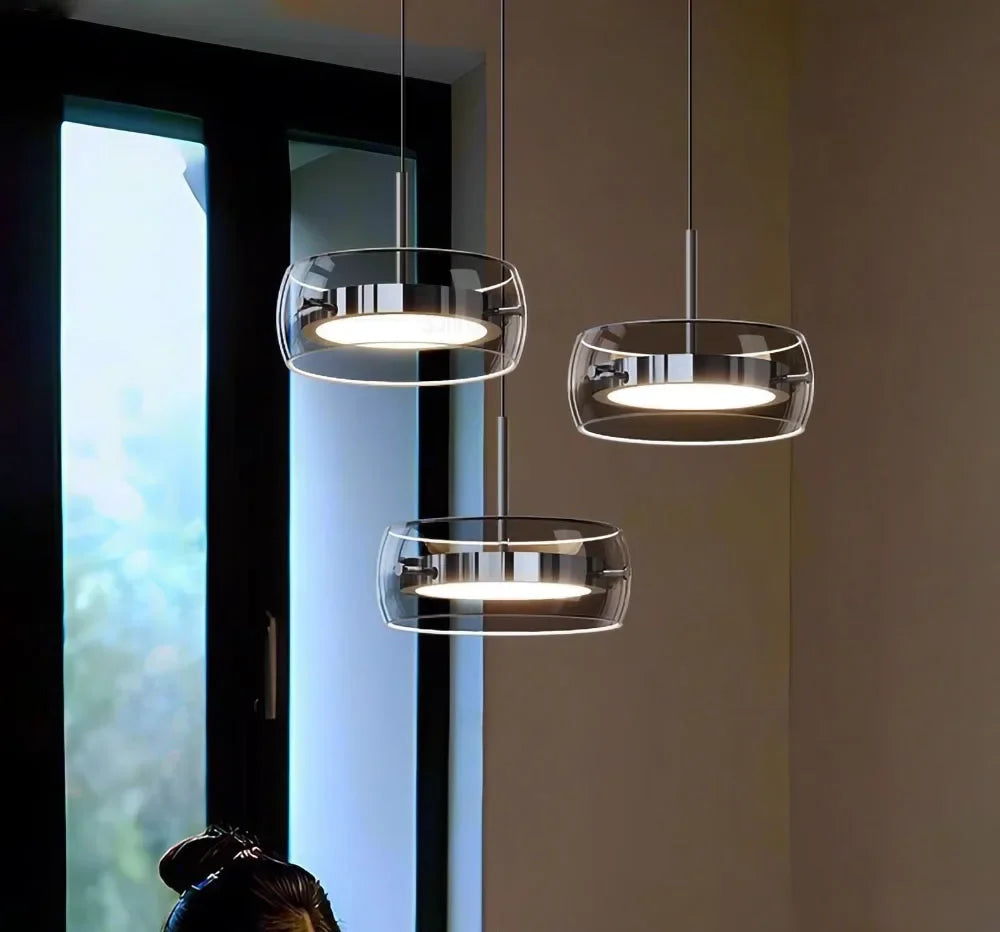 Three modern pendant lights with clear glass shades and chrome metal frames emitting warm indoor lighting