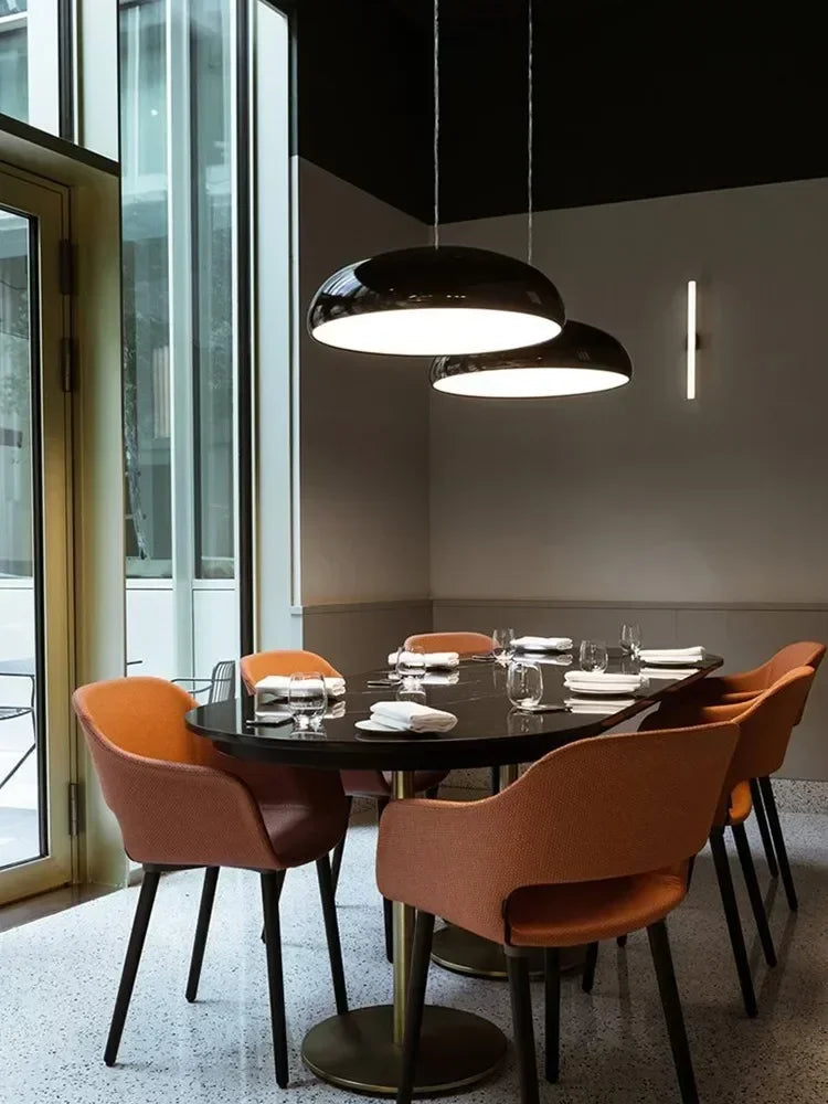 Black round dining table with sleek metallic legs surrounded by orange chairs under modern round aluminum pendant lights
