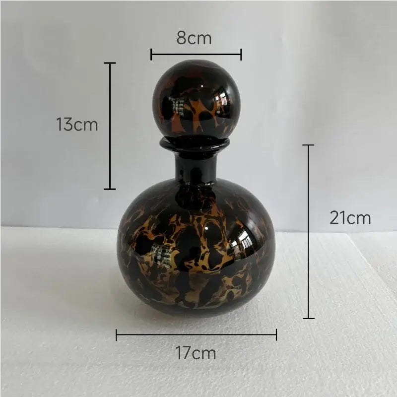 A glossy black glass perfume bottle with amber gold marbled patterns and spherical stopper in decorbites leopard texture glass style
