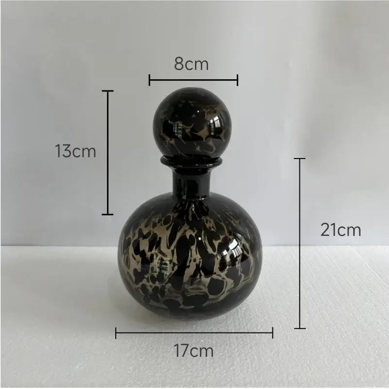 A glossy black glass perfume bottle with marbled gold and black leopard texture topped by a spherical stopper