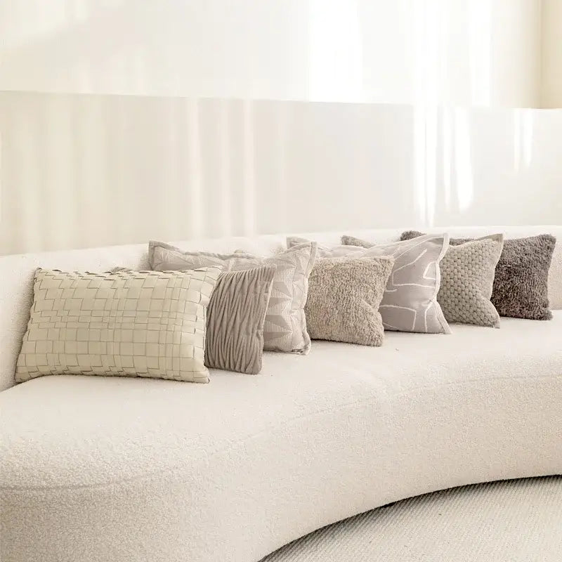 A collection of decorbites light grey coffee cushion covers with textured geometric patterns on an off-white sofa