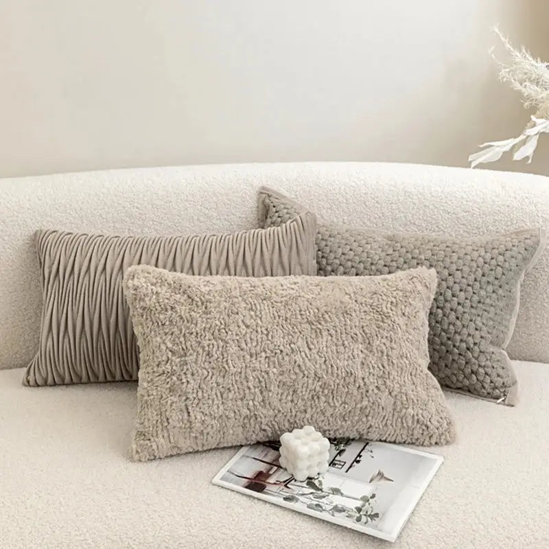Three beige textured throw pillows with ribbed fuzzy and knitted cushion covers on a soft white couch decorbites light grey