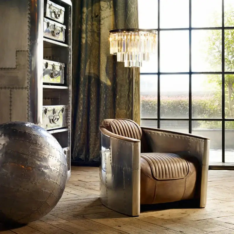 A sleek vintage-inspired armchair with metallic silver frame and tan leather upholstery next to decorbites gray crystal black standing lamp