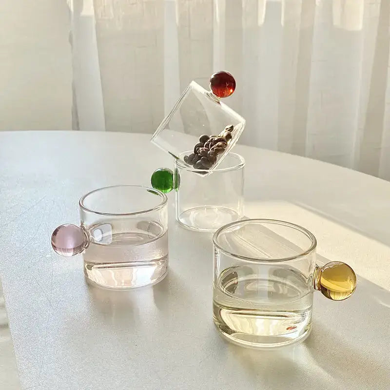 Clear glass espresso cups with colorful pink green and yellow spherical handles in a modern marble sphere set