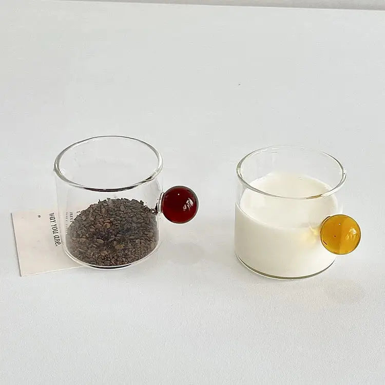 Two clear glass espresso cups with red and amber marble sphere handles, each holding a different beverage