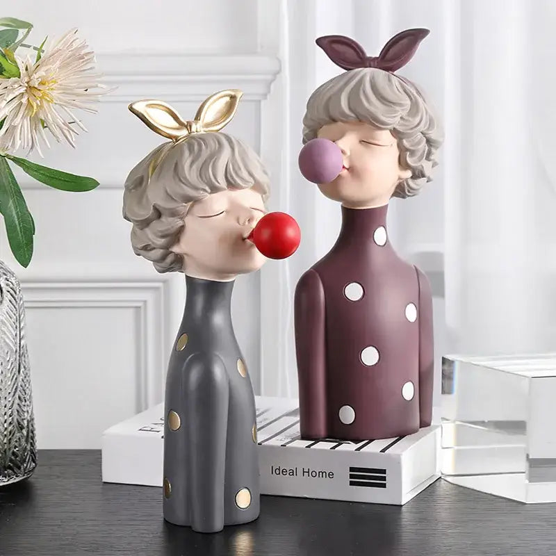Two whimsical resin bubble gum girl statues in gray with gold and maroon with white polka dots for bedroom decor
