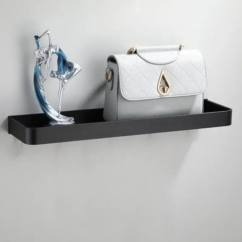 A sleek modern matte black aluminum corner shelf holds a silver and blue figurine beside a white quilted handbag