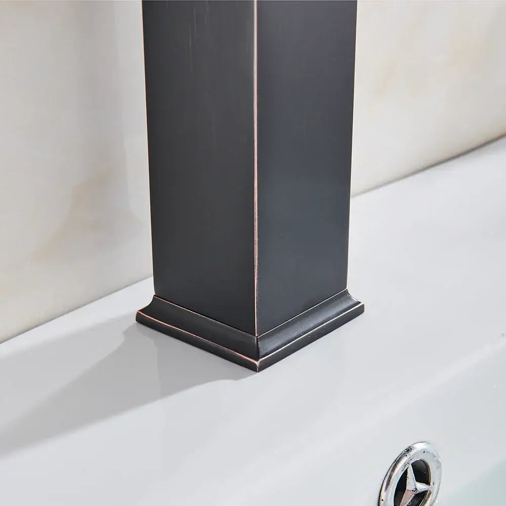 A sleek modern matte black basin mixer faucet with a rectangular column design and dark bronze metallic edges