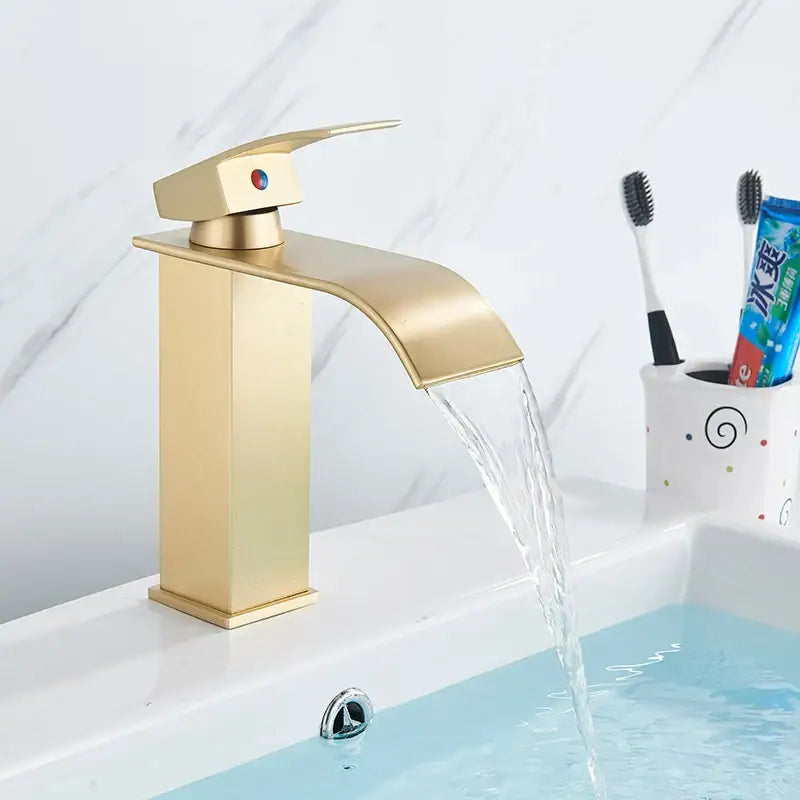 Gold-colored brass bathroom waterfall faucet with a sleek modern design and brushed finish for black brass bathroom decorbites