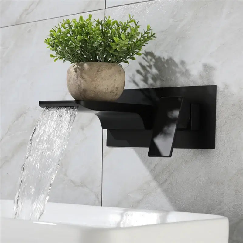 Modern matte black solid brass basin faucet with waterfall spout and integrated shelf holding textured beige pot