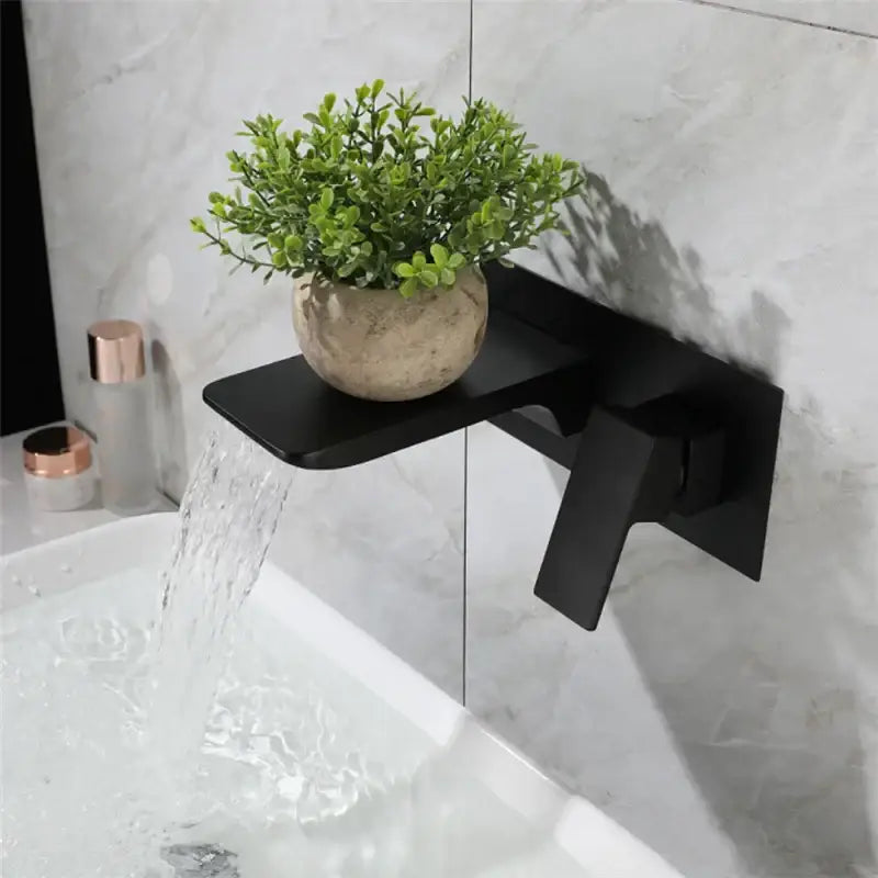 Modern matte black basin faucet with solid brass brushed gold accents and integrated shelf holding green foliage pot