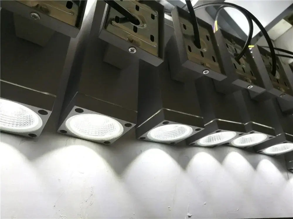 Row of modern matte black and silver outdoor wall lamps with rectangular LED sconces and circular white light fixtures