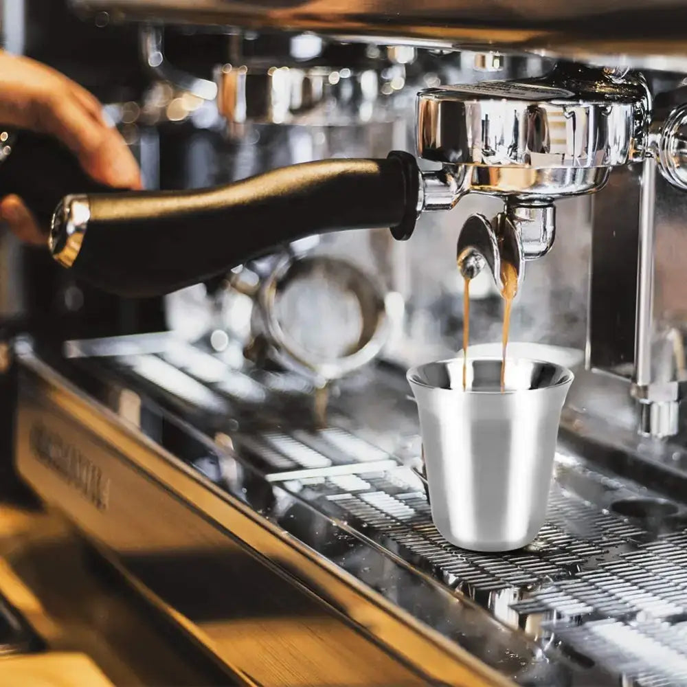 Shiny stainless steel double walled espresso cup catching dark coffee from espresso machine in modern matte set