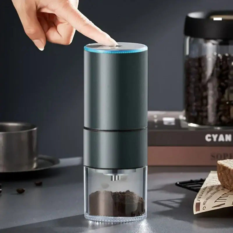 Modern matte gray electric bean grinder with dark green cylindrical body transparent base and glowing blue ring