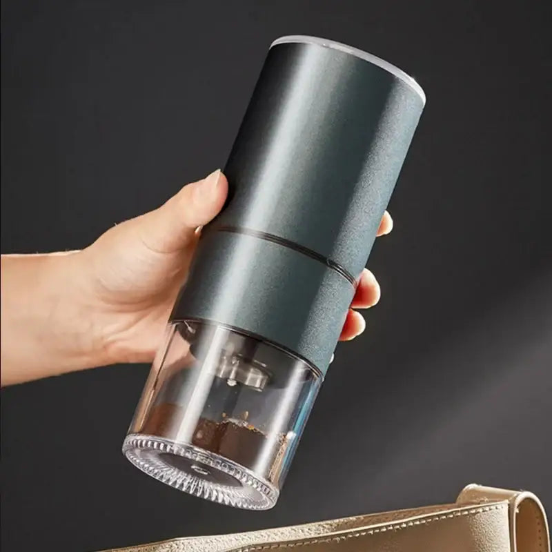 A modern matte gray electric bean grinder with a transparent base showing ground beans inside for kitchen use